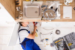 A plumber holding a wrench and standing next to a sink with water flowing out.