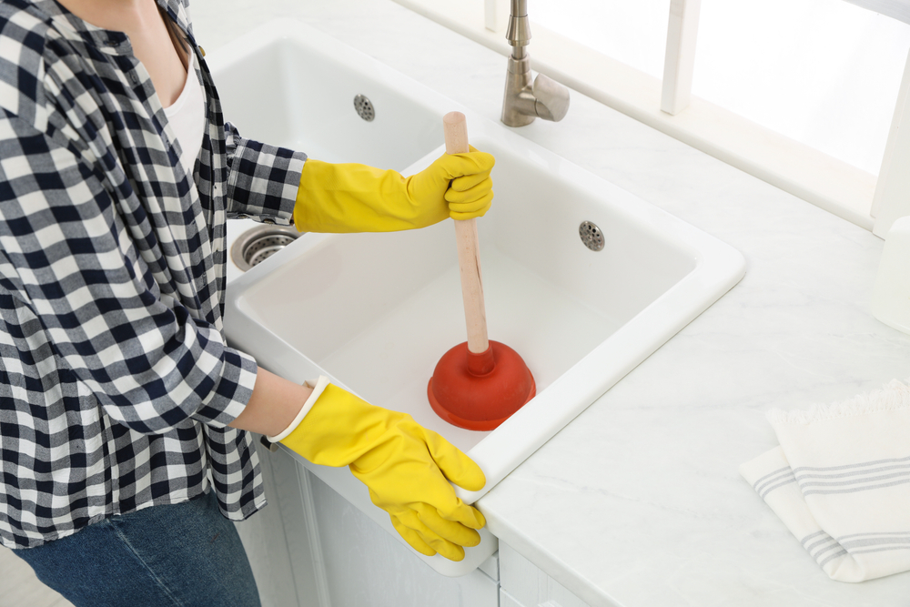 woman using plunger on clogged drain